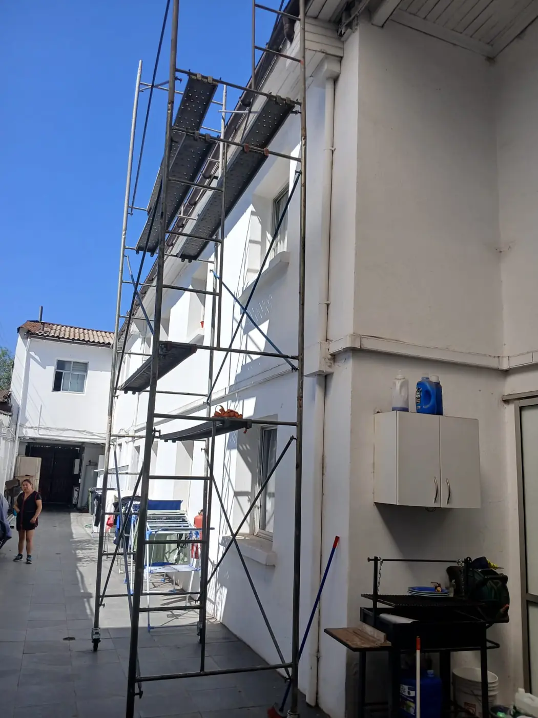 Andamio tubular con ruedas frente a fachada blanca en patio - Servicios Urgentes